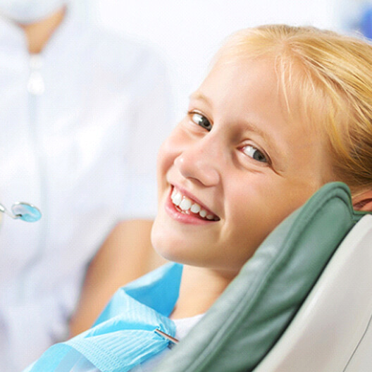 A young girl smiling while seated in the dentist’s chair preparing to see a kid’s emergency dentist in Palm Harbor