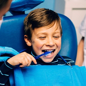 Child smiling while brushing their teeth in treatment chair