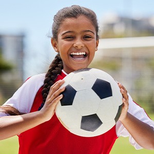 Child smiling while holding soccer ball on field