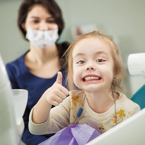 Child smiling while giving thumbs up in treatment room