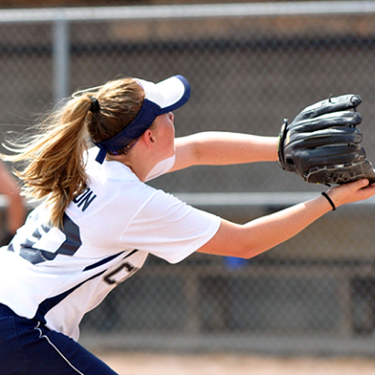 A female teenager playing softball and wearing a glove to catch the ball