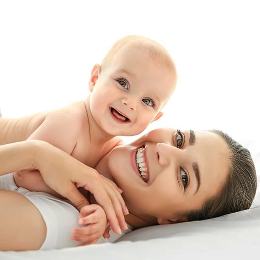 A mother lying on her back with her baby on her chest, both smiling after seeing a lip and tongue-tie dentist in Palm Harbor