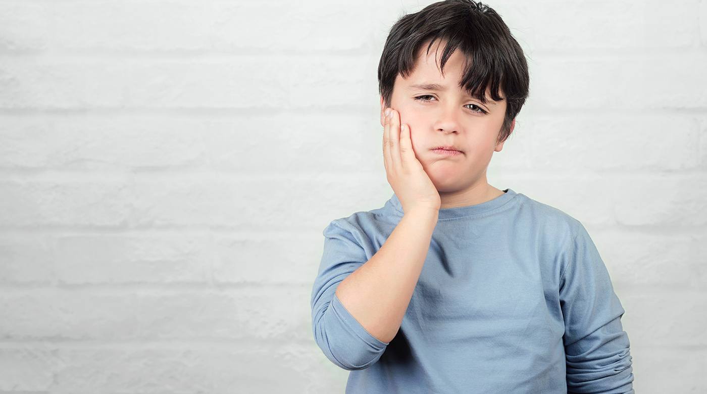Young boy standing in front of a brick wall with a toothache