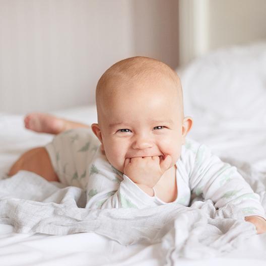 A baby lying on its stomach on a bed and chewing on its fingers because it is teething in Palm Harbor