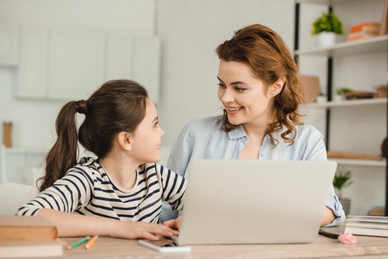 a mother and daughter smiling while seated at the table on a laptop