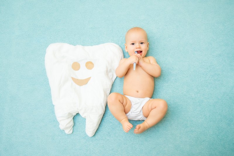 Baby with toothbrush lying next to tooth-shaped blanket