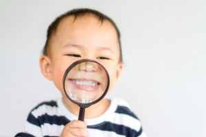 young child holding magnifying glass to teeth 