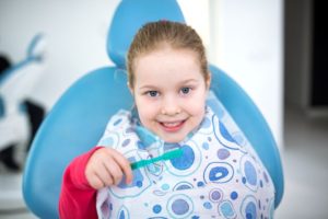 Happy child sitting in dentist’s chair, holding toothbrush