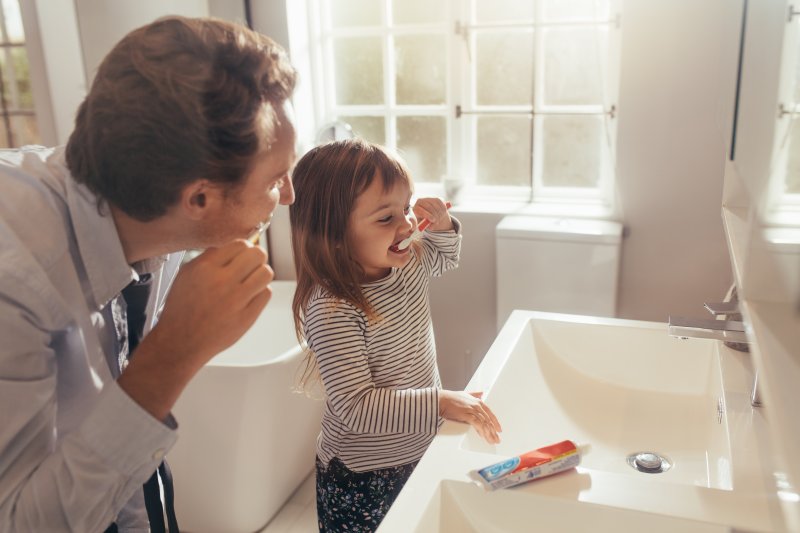 a parent and their child brushing their teeth