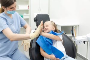 Girl with blond hair in dentist's chair high-fiving dentist wearing blue scrubs and mask with white gloves